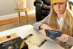 A woman sitting at a table reading through information from a murder mystery game from The Deadbolt Mystery Society.