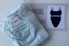 A light blue folded bralette and pair of underwear in a clear package, resting on top of a notecard included in the subscription