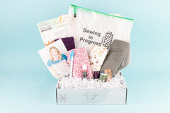 Open IndieStitch box featuring the Ivy Color-blocked Tee from Sinclair Patterns. Other objects in the box include fabric and project bag.