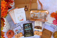 A cozy arrangement of fall-themed items in the Believer's Box VP, featuring socks, a candle, and a faith-inspired book