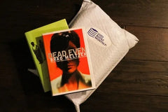 A stack of used books in front of a Used Books Monthly subscription box showcasing a book subscription service