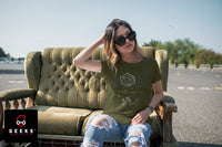 Lady sitting on a couch outside in a parking lot. She is wearing an olive green Dungeons and Dragons Shirt with an equation and 20 sided die