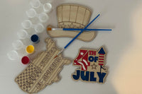 Three wooden patriotic shapes with 2 paint brushes and a paint sampler. One of the shapes is painted as an example.