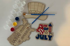 Three wooden patriotic shapes with 2 paint brushes and a paint sampler. One of the shapes is painted as an example.