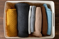 Overhead view of seven pieces of clothing. Clothing is neatly folded and organized in a cream colored bin. 