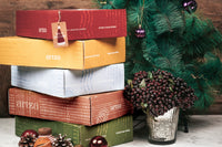 Colorful Artza subscription boxes stacked beside a festive green garland and decorative ornaments for Christmas