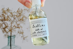 Hand holding the Bedtime Chamomile Bath Oil by Greenmade goods with dried baby's breath flowers in the background.