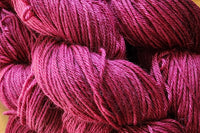 A close up of several skeins of Hand Dyed Baby Alpaca Sport Weight Yarn in a deep magenta colorway .