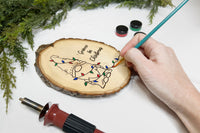 A hand adding paint to a Crate Club Project - the Christmas gnome wrapped in Christmas lights with letters that read "Gnome for Christmas"