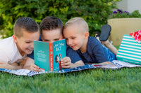 Two children reading books from Bookroo's Tween Book Club subscription on a colorful rug with additional books nearby