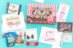 A chocolate-themed subscription box. Items include novelty pen, earrings, holiday greeting card, chocolate spoons, and snacks.