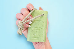 Hand holding a green bar of the Lemon Verbena Exfoliating Soap on a rope with natural knotted hemp rope.