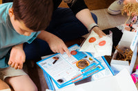 Child and parent exploring a BāKIT Box baking kit, reading the recipe card and organizing pre-measured ingredients for a hands-on baking act