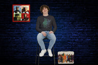 Young man wearing an Avengers Long Sleeve Tee and has a tin lunch box next to him on the floor and an Avengers clock on the wall.