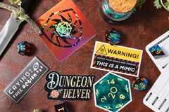 Five stickers scattered with a red 20 dice, a warning sticker, a crying is a free action sticker, a dungeon delver sticker, and a green d20.