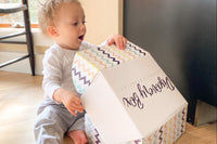 Adorable one year old baby opening up a baby discovery box and has a look of surprise on his face as he views the great books and toys