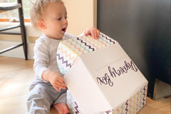 Adorable one year old baby opening up a baby discovery box and has a look of surprise on his face as he views the great books and toys