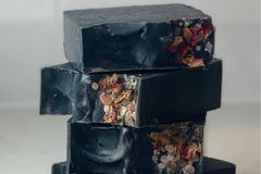 Black bars of soap stacked on top of each other with decorative rose and pink salt tops. This is the Tea Tree and Charcoal soap. 