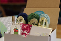 Yarn Shop Mystery Box featuring three skeins of Frog Tree Alpaca Sport yarn in green, navy, and teal with craft accessories