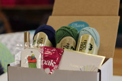 Yarn Shop Mystery Box featuring three skeins of Frog Tree Alpaca Sport yarn in green, navy, and teal with craft accessories
