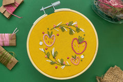Embroidery project featuring three strawberries stitched in shades of pink and surrounded by vines in shades of green, white, and pink.