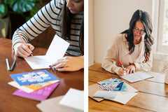two ladies sitting down with an assortment of greeting cards and envelopes in front of them writing a note inside one of them
