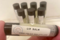 In the foreground, a labeled lip balm is held close to the camera, while a cluster of similar-looking lip balms stand in the background.