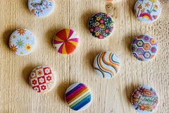 Spring 2023:  Seventies  theme one inch buttons in psychedelic colors and patterns such as rainbows and flowers.