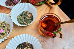 Up-down: Fruitful Foraging, Detox Bitter, Cramp Reliever, and Immunity Dark teas. To the right is a cup of black tea with a gold spoon in it