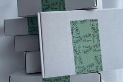 A stack of six boxes pilled up high.  They are white with a green that road trip mom shipping trap on them. 