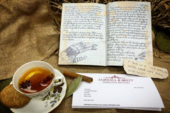 Box one contains a diary, scrap of paper, personalised letter and a leaf, shown with a cup of tea and biscuit