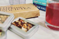 The Sipping Societea Loose leaf tea subscription box with tea tins next to fruity red iced tea and books.