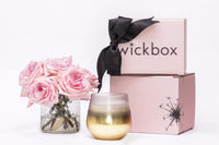 A luxurious candle from the Wickbox monthly subscription box beside floral accents and candle care tools