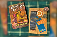 Book titled Legends and Lattes by Travis Balder laying next to wrapped book with bookmarks and items, on top of green background