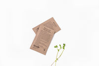 Two seed packets sit on top of each other with a white background. They are brown paper. One says "alfalfa" and the other "broccoli".
