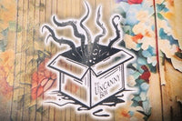 The Uncanny Box logo on the back of story Welcome Home with colored wallpaper in the background. A box with tentacles bursting from the top.