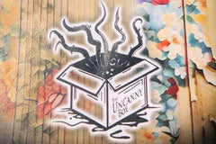 The Uncanny Box logo on the back of story Welcome Home with colored wallpaper in the background. A box with tentacles bursting from the top.