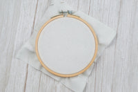 white counted cross stitch fabric in size 14 count mounted inside wood embroidery hoop on distressed wood background