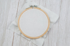 white counted cross stitch fabric in size 14 count mounted inside wood embroidery hoop on distressed wood background