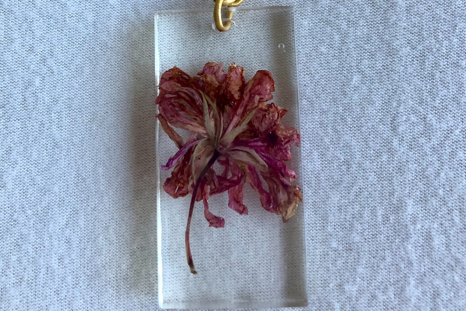 This necklace features an adjustable leather cord and a pendant that was hand made with a preserved flower that was cast in resin. 