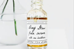 The Day Glow Serum by Greenmade goods. A bottle with golden serum dripping down the label. A clear vase with water in the background.