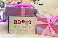 A Girl Gang Strong subscription box with pink wrapped gifts on top and next to it, all on a white, fluffy rug.