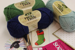 Yarn Shop Mystery Box featuring three skeins of Frog Tree Alpaca Sport yarn in green, navy, and teal with craft accessories