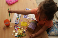 Young girl painting a treasure chest craft from the Little Dreamers Club monthly subscription box with colorful "loot" displayed