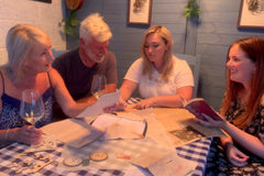 Mother and father play with two children together at the kitchen table, picture shows wooden cogs, a vintage diary and some photocopies