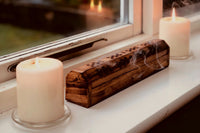 white window ledge with two white pillar candles that are both lit and in between in a wood carved box with smoke filtering out