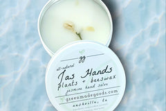 An open 2 oz tin of Jas Hands by Greenmade goods showcasing jasmine scented hand salve with dried jasmine buds.
