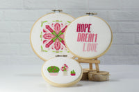 hope dream love words in pink and red cross stitch with flower and three potted cross stitch plants in hoop