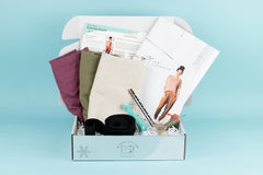 Open IndieStitch box featuring the Arenite Pants from Sew Liberated. Linen fabrics with sewing tools are displayed in the box.