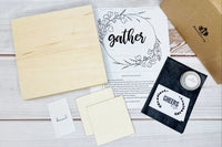Ingredients of a box laid out on the table with a pattern that says "Gather", a sawtooth hanger, wood finish, etc.
